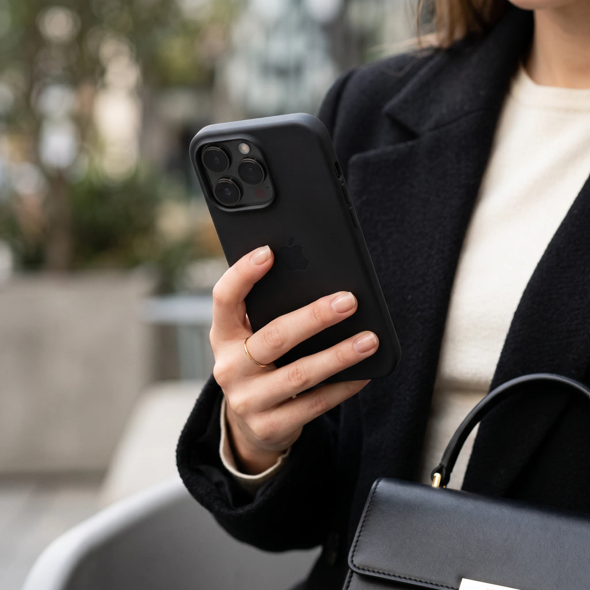 Siyah lansman silikon iPhone kılıf, şık siyah palto ve çantayla şehirde kullanımda